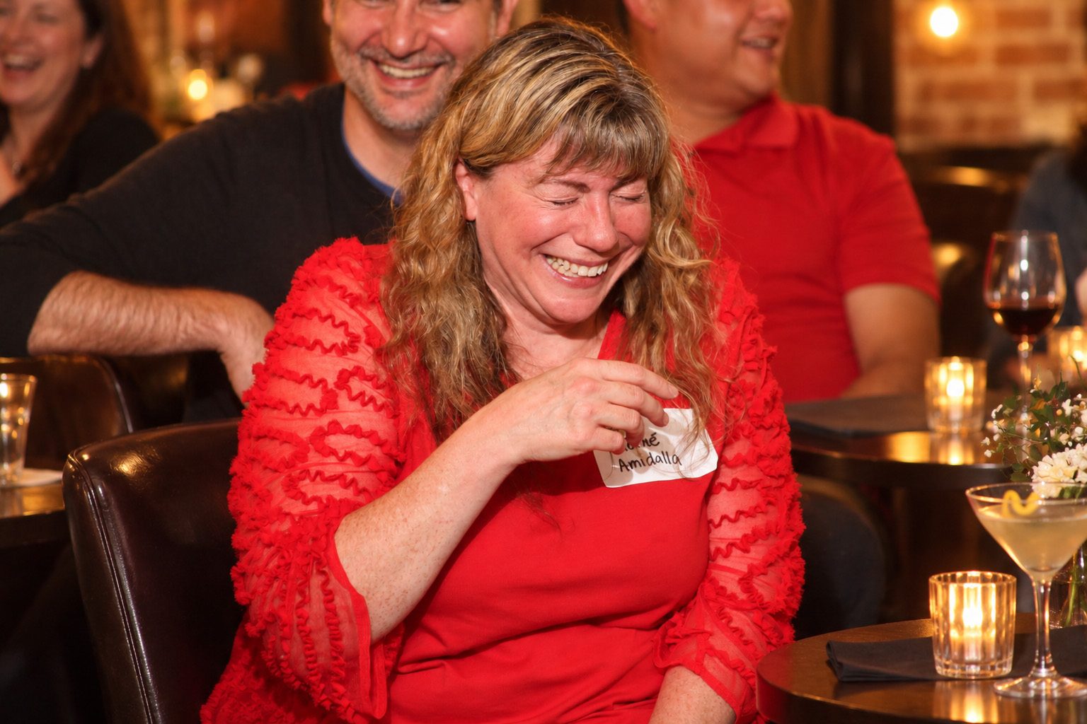 A guest in a red dress laughs at a candlelit table